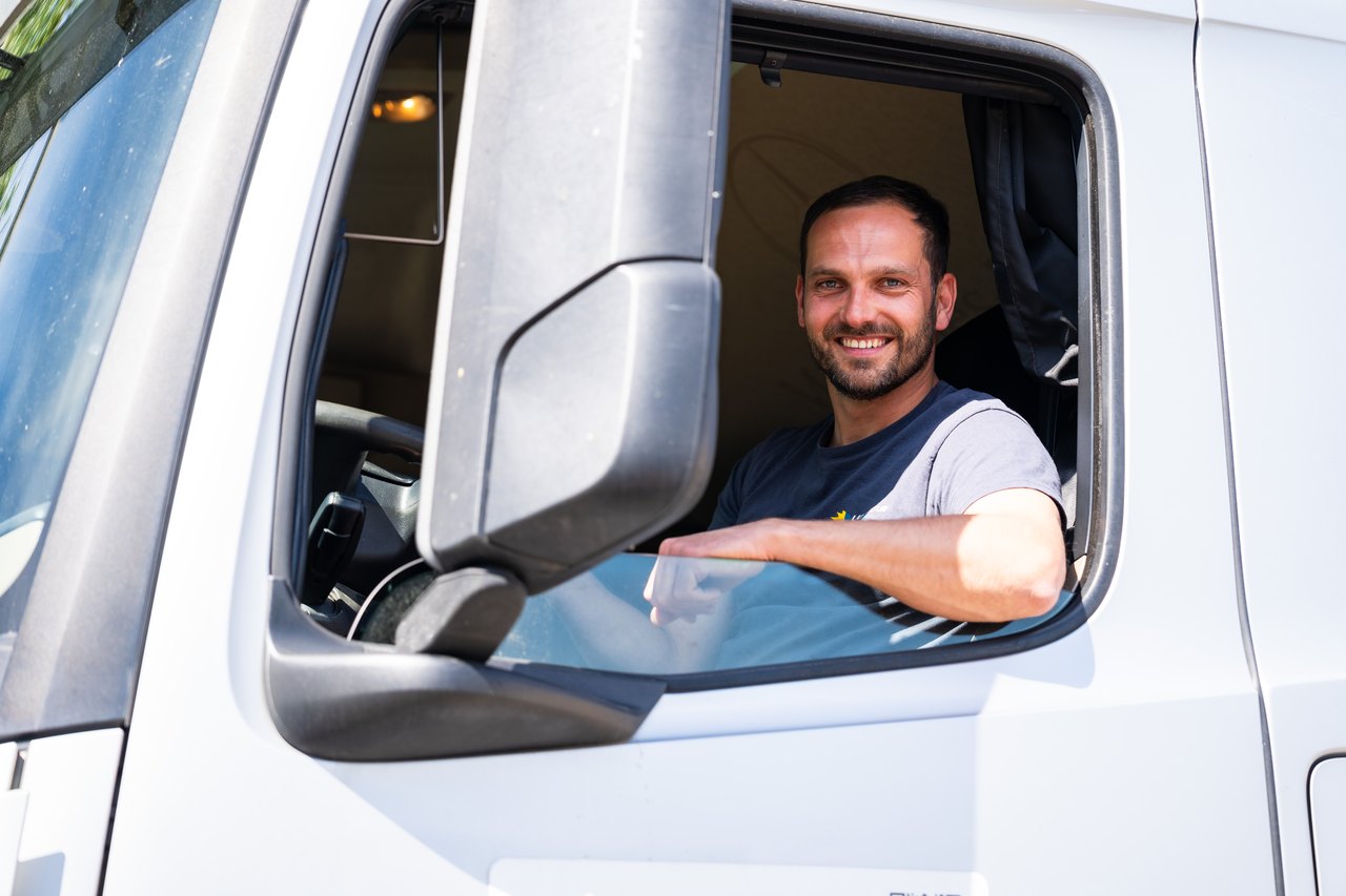 Ein lächelnder LKW-Fahrer schaut aus dem offenen Fenster seines weißen Lastwagens.
